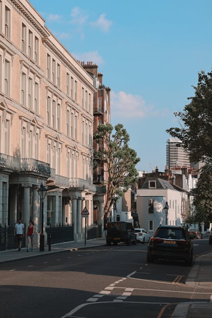 The image depicts a residential street scene outside a row of traditional multi-storey London townhouses with beige facades, decorative window frames, and iron balconies. The street features parked ca
